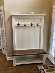 a white bench with two hooks on the back and an open door to another room