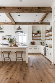 an open kitchen with white cabinets and wooden beams on the ceiling, along with bar stools