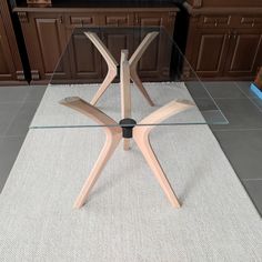 a glass table with wooden legs in the middle of a kitchen area, next to brown cabinets