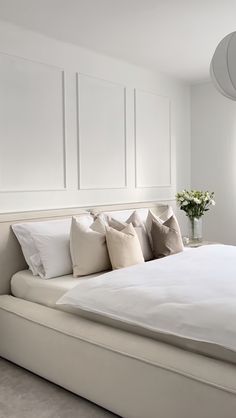 a bed with white sheets and pillows next to a vase filled with flowers on top of it