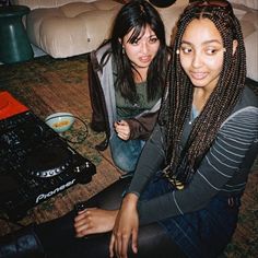 two young women sitting on the floor next to a dj's mixer and mixing equipment