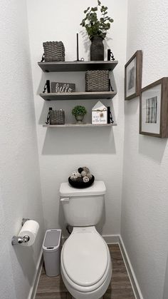 a white toilet sitting in a bathroom next to a shelf filled with pictures and plants