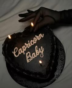 a heart shaped cake with the words capricon baby written on it and lit candles