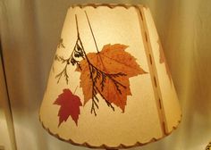 a lamp that is sitting on a table with leaves painted on the lampshade