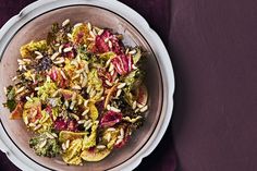 a white bowl filled with food on top of a purple table cloth next to a wooden spoon