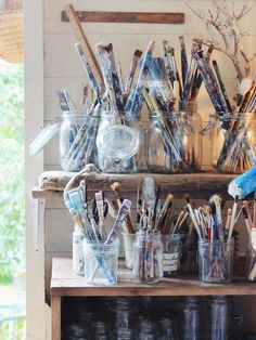 an assortment of paint brushes and jars on a shelf