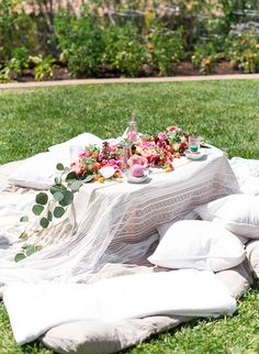 a table with flowers and candles is set on a blanket in the grass