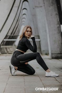 a woman sitting on the ground wearing black and grey workout clothes with her hands behind her head