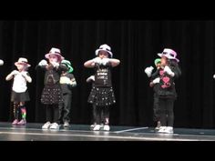 several children are performing on stage with their hands in the air and one child is wearing a hat