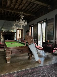 a shirtless man leaning on a pool table in a room with chandeliers