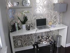 a white desk topped with a laptop computer next to a wall covered in mirrors and flowers