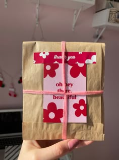 someone is holding up a gift wrapped in brown paper with red and white flowers on it