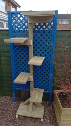 a wooden shelf in the middle of a garden with blue trelliss behind it