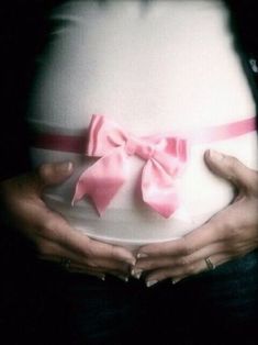 a pregnant woman holding a plate with a pink bow on it's belly in front of her stomach