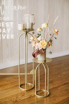 two metal plant stands with flowers in them on a wooden floor next to a wall