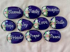 purple painted rocks with white flowers and words on them that say,'happy, love, peace, hope, family, joy, and smile