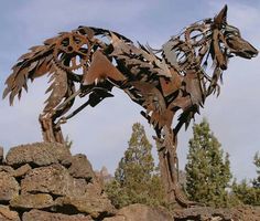 a sculpture of a dog made out of metal on top of rocks and trees in the background