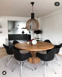 a round wooden table surrounded by black chairs in a living room with white walls and flooring