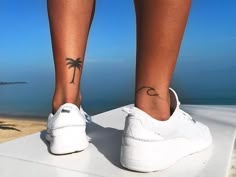 a woman's foot with a small palm tree tattoo on her left ankle and the ocean in the background