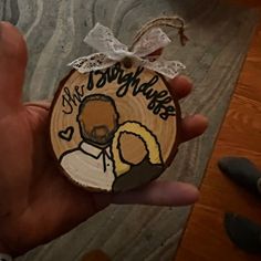 someone is holding up a wooden ornament with an image of a man and woman on it