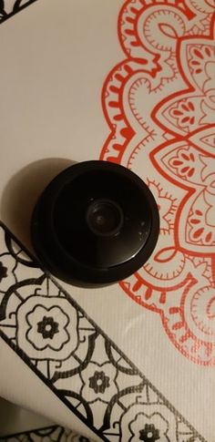 a black button sitting on top of a white and red wallpaper covered in paisley designs