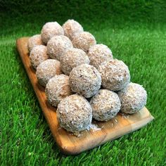 a wooden tray filled with chocolate covered donuts on top of green grass