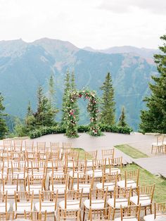 an outdoor ceremony set up with wooden chairs and flowers on the mountain side, surrounded by greenery