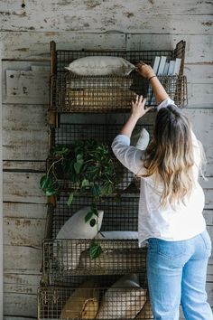 a woman standing in front of a shelf filled with plants and other animal cages on the wall