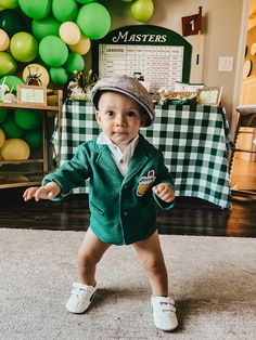 a little boy in a green suit and hat standing on the floor with his arms out