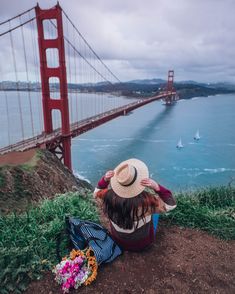 a woman sitting on the ground with her hat over her head looking out at the water