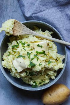 mashed potatoes with butter and parsley in a bowl next to a wooden spoon