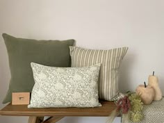 some pillows are sitting on a wooden table next to a vase and two pumpkins