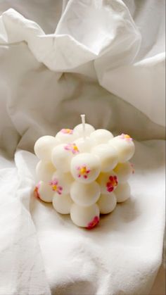 a white candle with pink and yellow sprinkles sits on a bed sheet