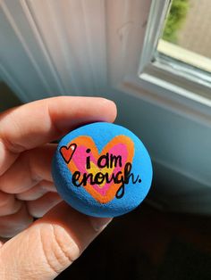 a person holding a rock with the words i am enough painted on it in front of a window