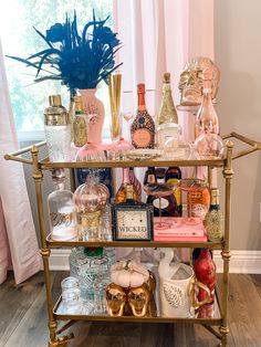 a gold bar cart filled with lots of bottles and glasses on top of a hard wood floor