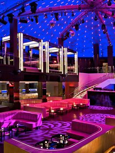 the inside of a building with purple lighting and tables in front of large chandeliers