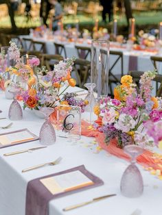 the table is set with many different types of flowers and place settings for guests to sit at