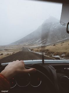 a person driving a car on a road with mountains in the background and foggy weather