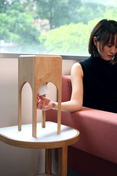 a woman sitting on a pink couch next to a wooden table with a doll house in it