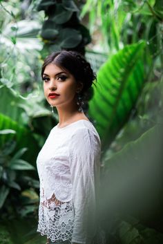 a woman standing in front of green plants and trees with her eyes closed to the camera