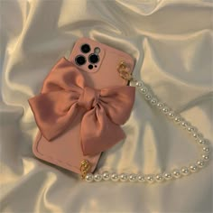 a cell phone with a pink bow and pearls on the side sitting on a white satin surface