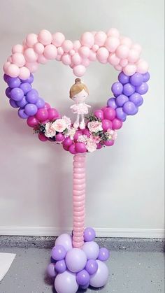 a balloon arch with a doll on top and flowers in the middle, surrounded by balloons