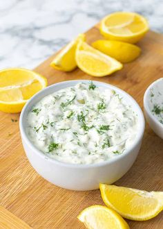 two bowls of dip surrounded by lemons on a cutting board