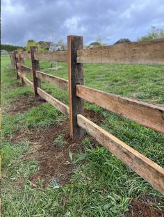 a wooden fence with grass and dirt in the foreground, on a cloudy day