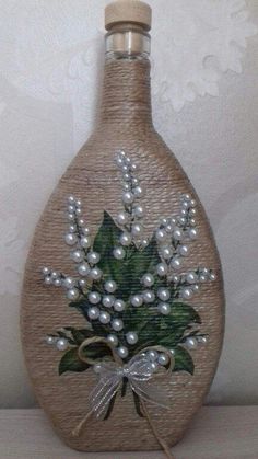 a bottle decorated with pearls and flowers on top of a wooden table next to a wall