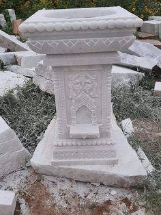 a white statue sitting on top of a pile of cement blocks next to grass and flowers