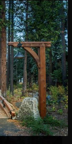 a wooden bench sitting in the middle of a forest next to a stone wall and tall trees