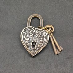 a heart shaped lock with two keys attached to it on a gray surface, the key is in the shape of a lion's head