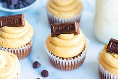 three cupcakes with peanut butter frosting and chocolate on top, next to milk