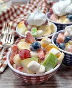 three bowls filled with fruit salad on top of a wooden table next to a fork